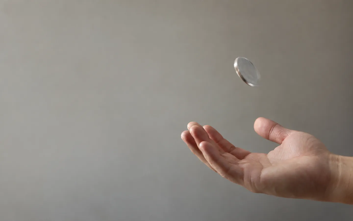 A silver coin caught in mid-air above an open hand, slightly blurred as it turns, against a soft plain background